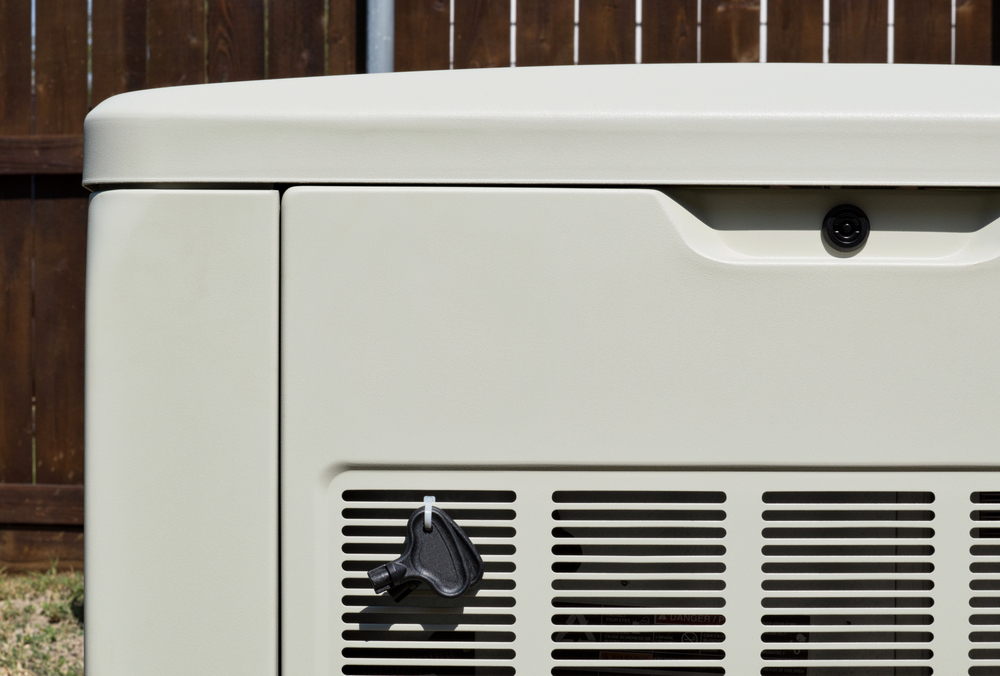 Close-up of the side of a beige outdoor generator with a vent and a black handle. A wooden fence is visible in the background.