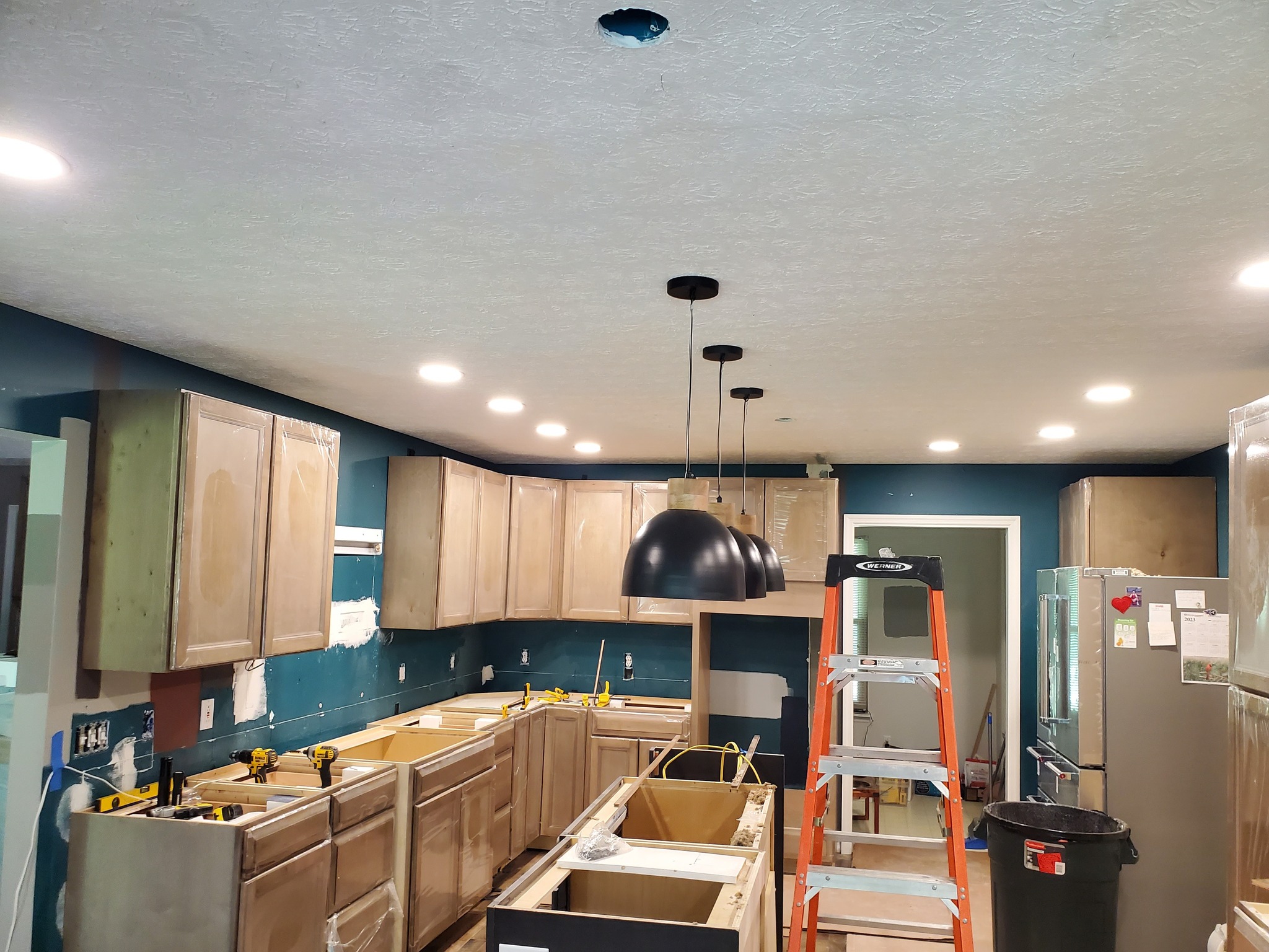 Kitchen under renovation with unpainted cabinets, a step ladder, and pendant lights installed.