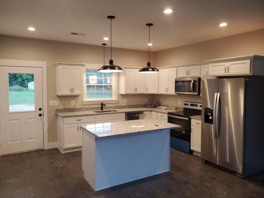 Modern kitchen with white cabinets, stainless steel appliances, and granite countertops. An island with pendant lights is in the center, and there is a window above the sink.