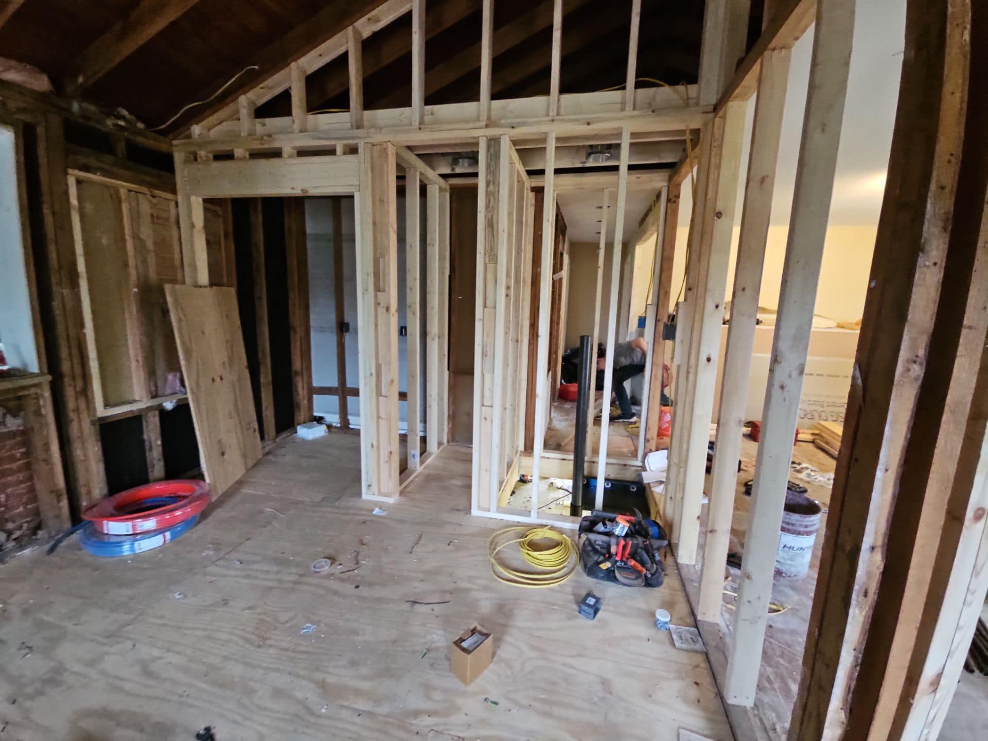 A room under construction with exposed wooden framing, electrical wiring, and construction tools scattered around.