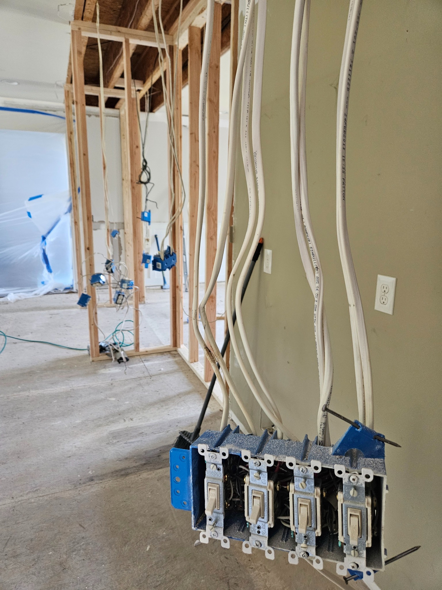 Electrical switches and wiring exposed during a residential renovation. Walls are partially framed and plastic sheeting is visible in the background.